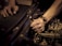 Hands working on a car engine, one grasping a wrench while the other steadies radiator fins. The scene is focused on the forearms and tools, highlighting mechanical components.
