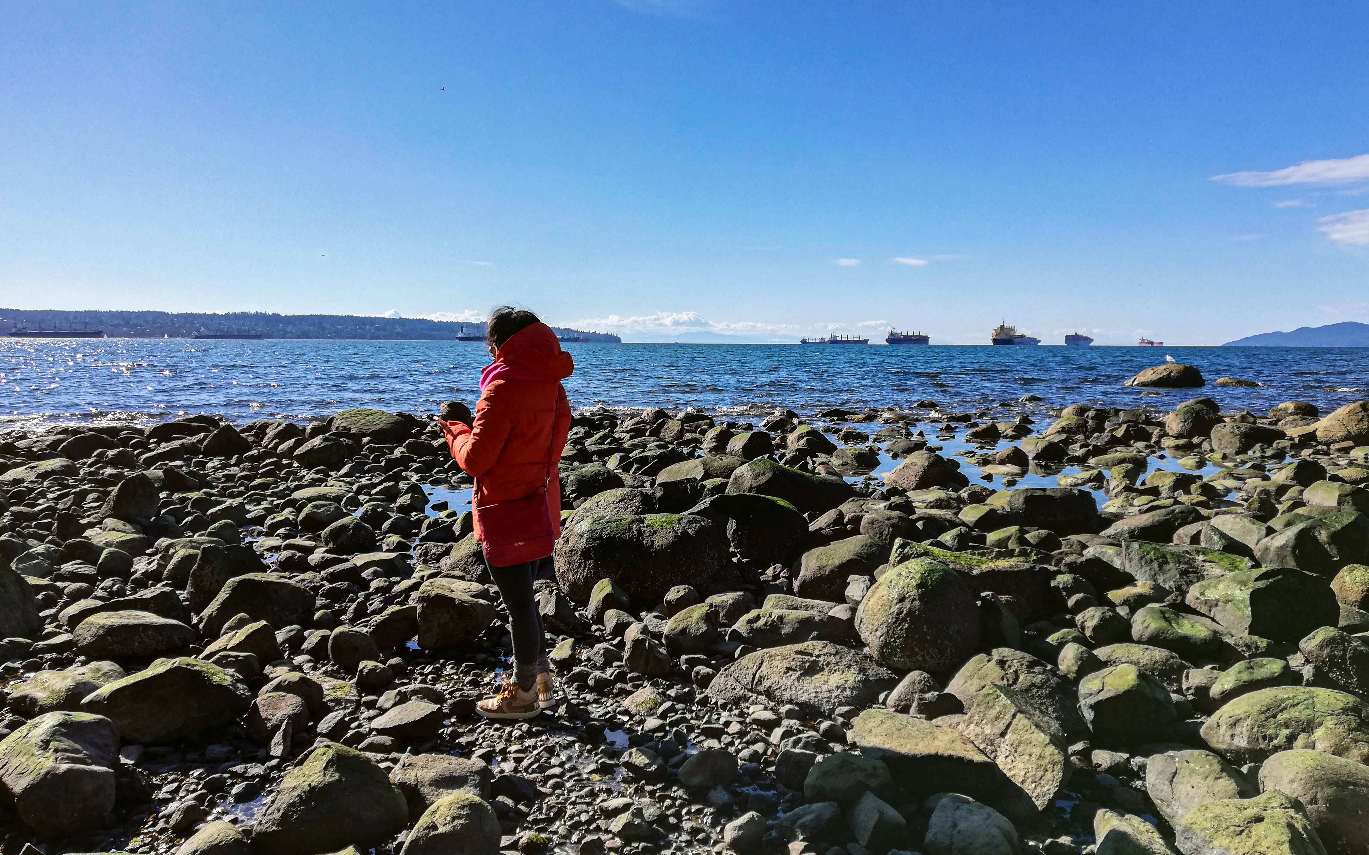woman in red jacket and black pants standing on rocky shore during daytime