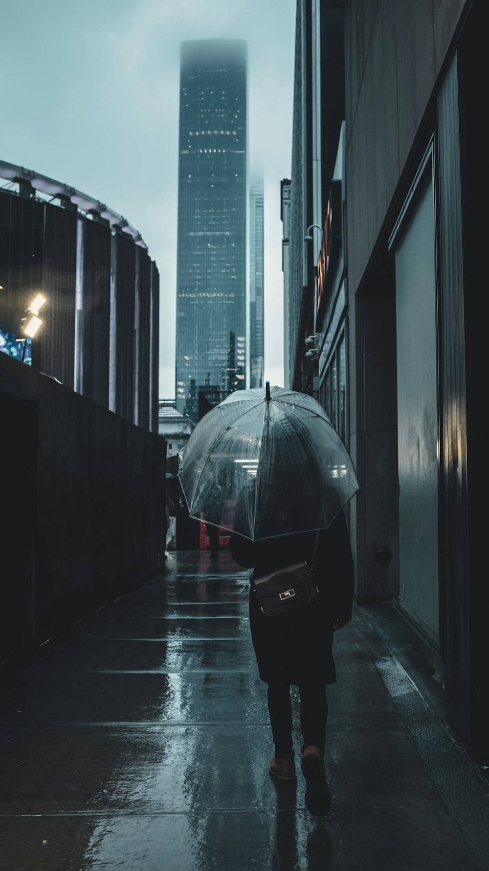 person in black jacket holding umbrella walking on sidewalk during daytime