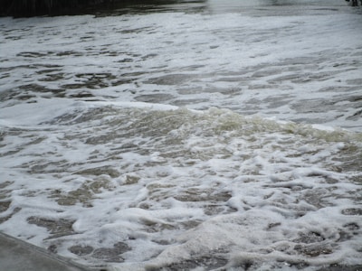 Foamy water with ripples on a water body, suggesting movement, possibly from a waterfall or rapid flow.