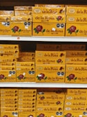 Shelves stacked with multiple boxes of 'de la Rosa' products, featuring a prominent rose logo and clear branding on yellow packaging.