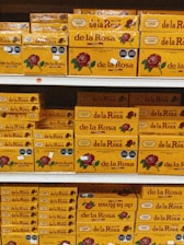 Shelves stacked with multiple boxes of 'de la Rosa' products, featuring a prominent rose logo and clear branding on yellow packaging.