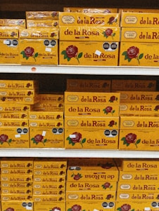 Shelves stacked with multiple boxes of 'de la Rosa' products, featuring a prominent rose logo and clear branding on yellow packaging.