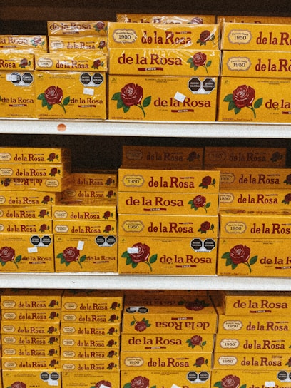 Shelves stacked with multiple boxes of 'de la Rosa' products, featuring a prominent rose logo and clear branding on yellow packaging.