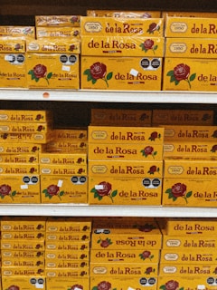 Shelves stacked with multiple boxes of 'de la Rosa' products, featuring a prominent rose logo and clear branding on yellow packaging.