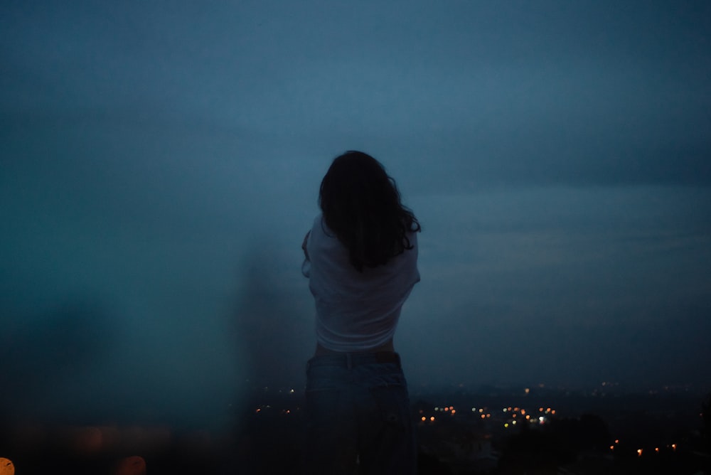 donna in camicia bianca e pantaloni neri in piedi in cima all'edificio durante la notte