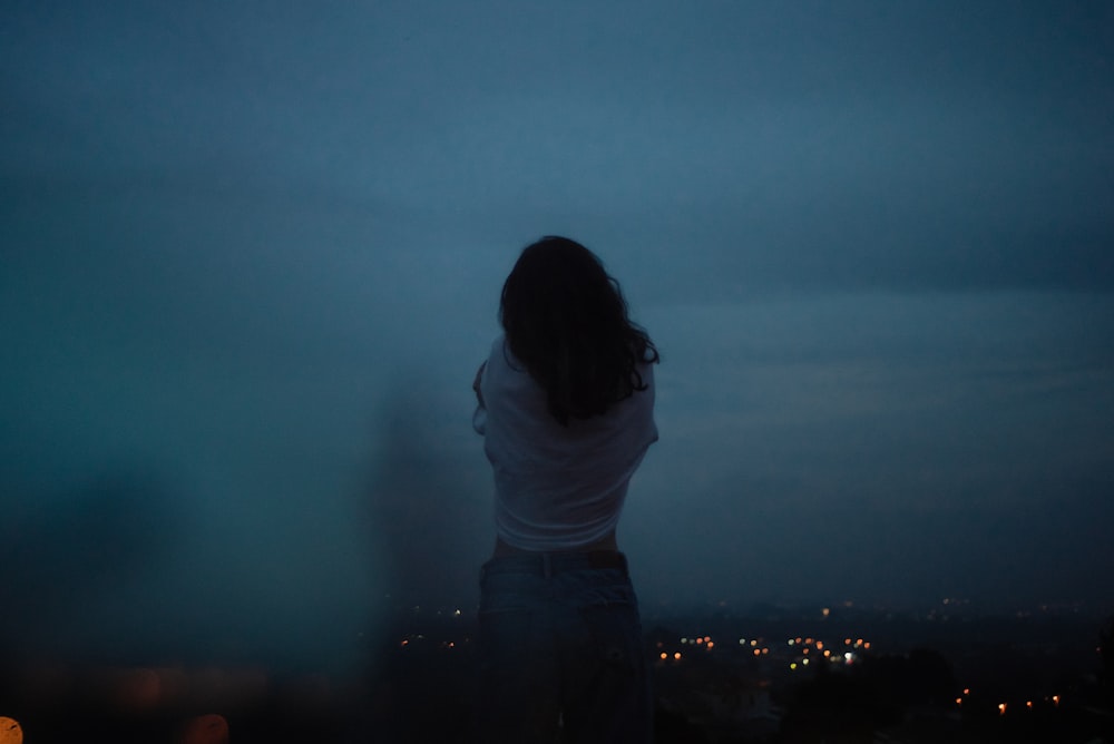 woman in white shirt and black pants standing on top of building during night time