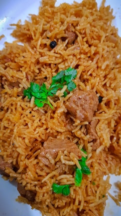 A plate filled with golden-brown rice mixed with chunks of tender meat, garnished with fresh green coriander leaves.