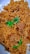 A plate filled with golden-brown rice mixed with chunks of tender meat, garnished with fresh green coriander leaves.