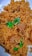 A plate filled with golden-brown rice mixed with chunks of tender meat, garnished with fresh green coriander leaves.