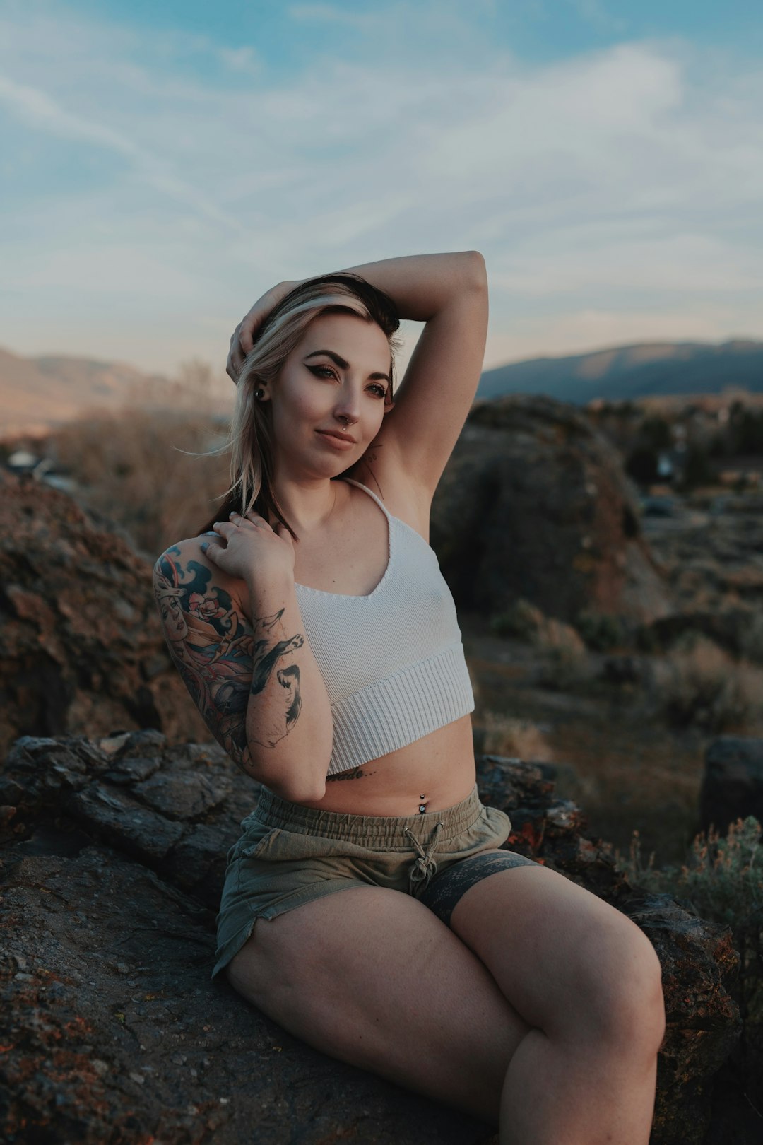 woman in white tank top and blue denim shorts sitting on rock during daytime