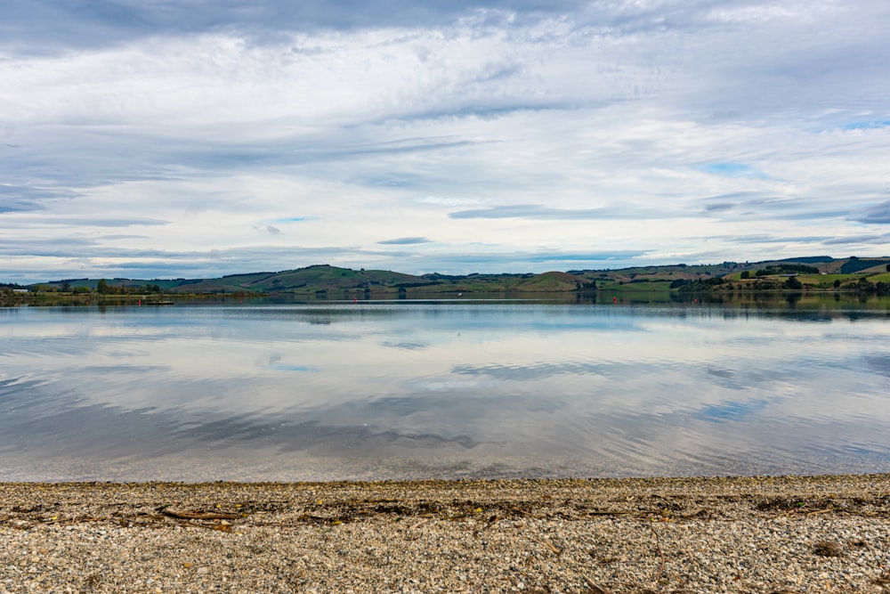 body of water near green trees under cloudy sky during daytime