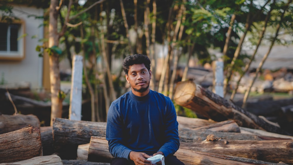 man in blue sweater sitting on brown log during daytime