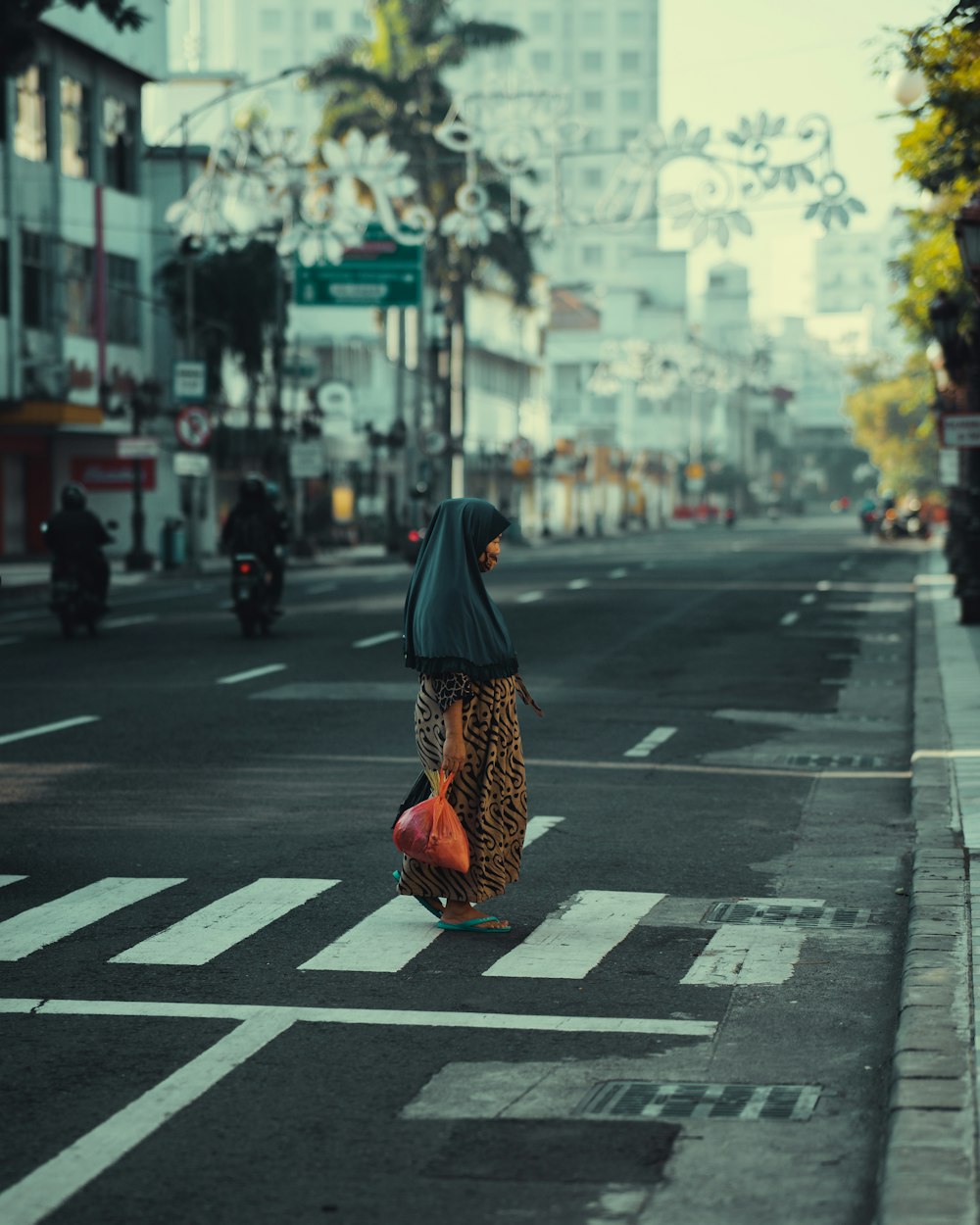 검은 히잡과 주황색 드레스를 입은 여자가 낮 동안 보행자 전용 도로를 걷고 있다