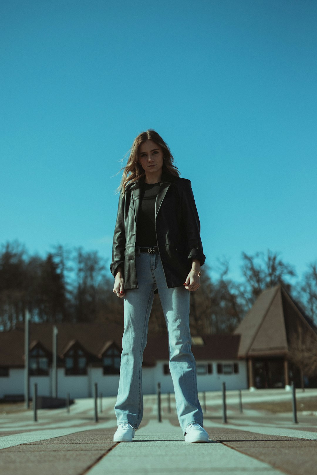 woman in black leather jacket and blue denim jeans standing on brown wooden dock during daytime