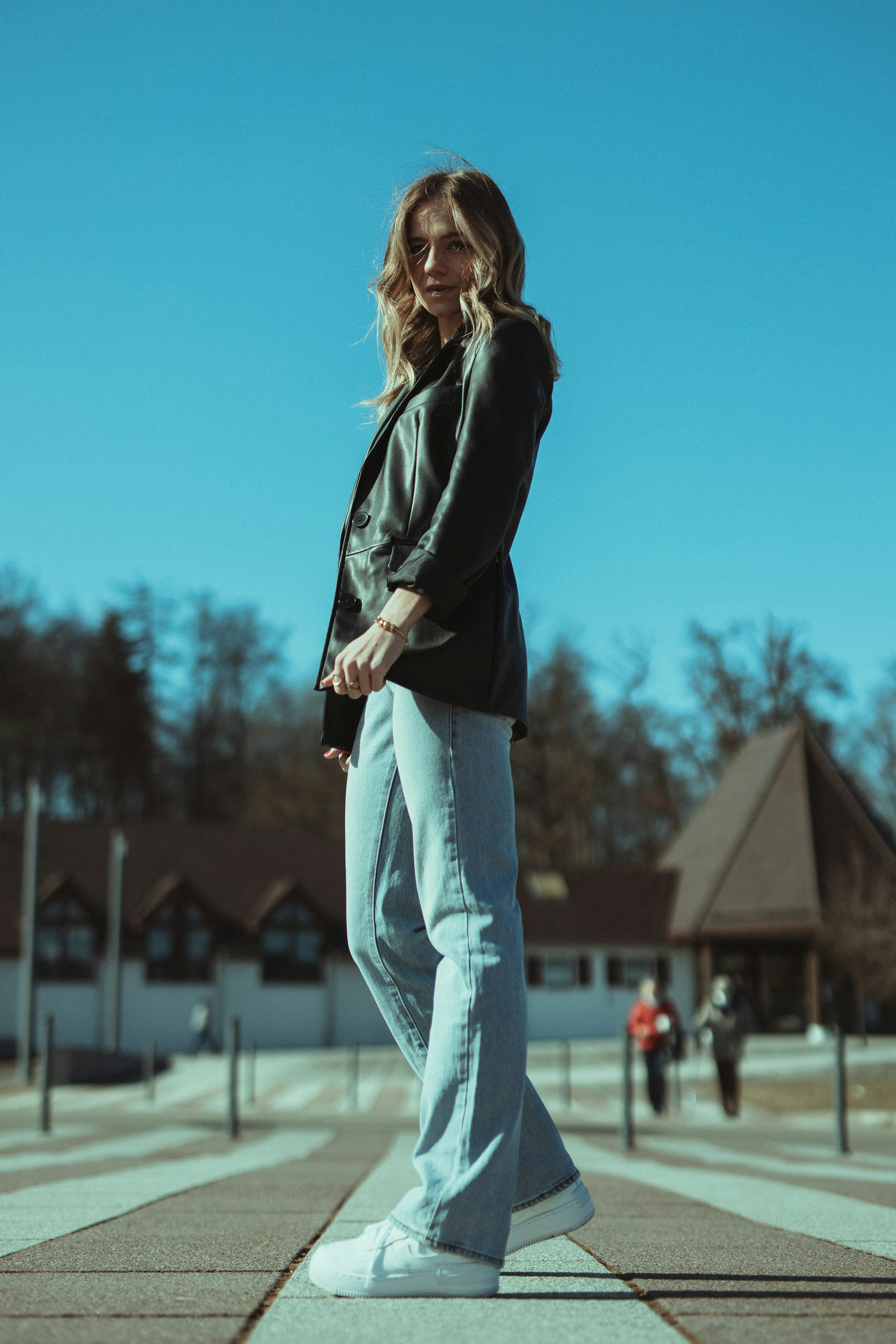 woman in black leather jacket and blue denim jeans standing on field during daytime