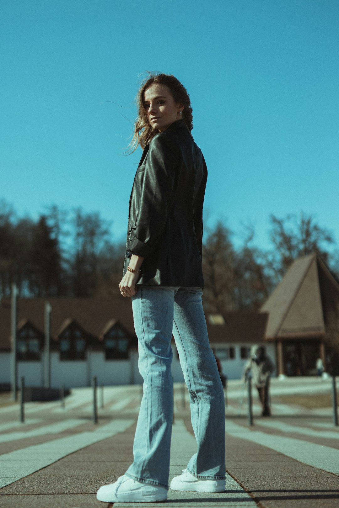 woman in black leather jacket and blue denim jeans standing on gray concrete floor during daytime