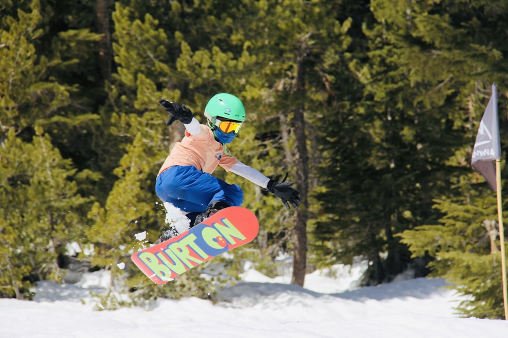 man in blue jacket and red helmet riding red snowboard on snow covered ground during daytime