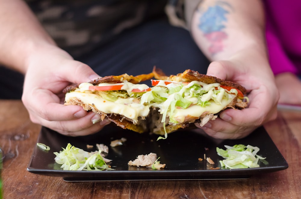 person holding burger with lettuce and tomato