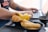 A person typing on a laptop, with a variety of pastries and snacks in black bowls in the foreground. The snacks include empanadas, tequeños, and what appears to be corn arepas. The person has tattoos on their arm and is wearing a casual shirt.