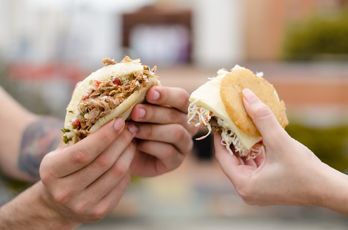 Two friends holding stuffed arepas, one arm tattooed