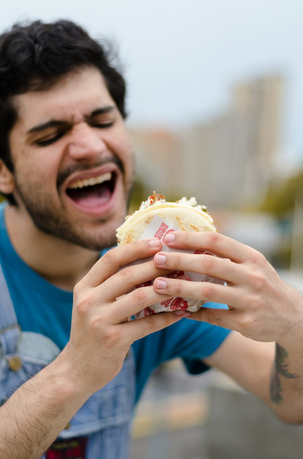 hombre con camisa azul de cuello redondo sosteniendo una hamburguesa