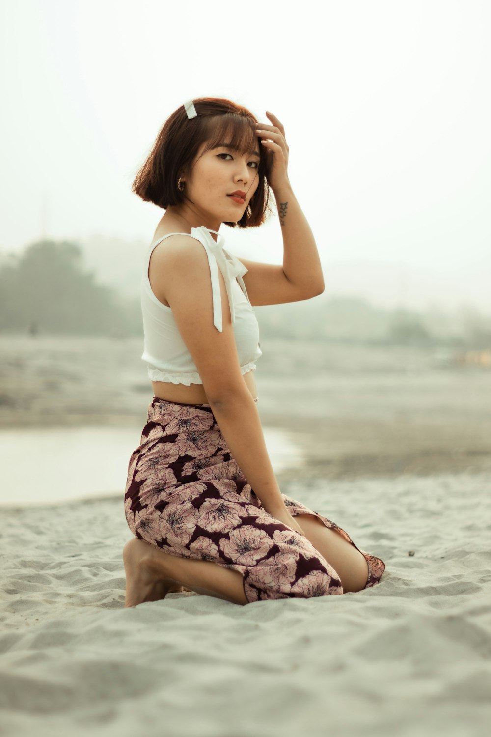 woman in white tank top and purple and white floral skirt sitting on beach shore during
