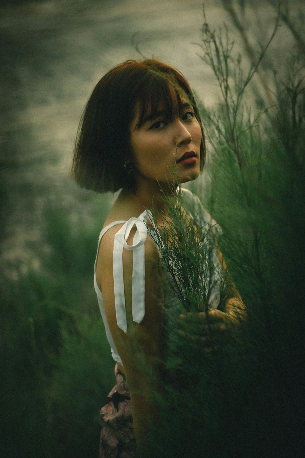 woman in white tank top standing near green trees during daytime