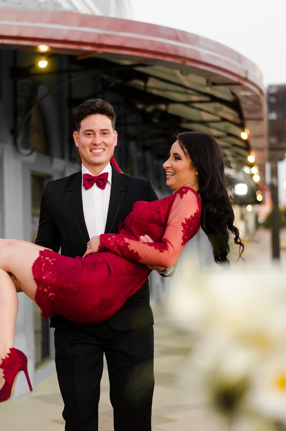 man in black suit hugging woman in red dress