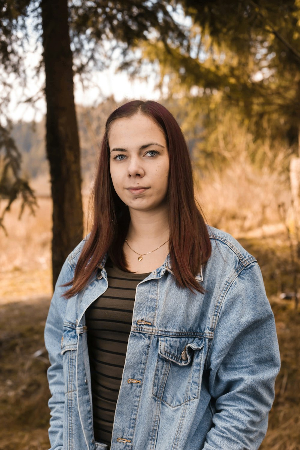 woman in blue denim jacket standing near brown trees during daytime