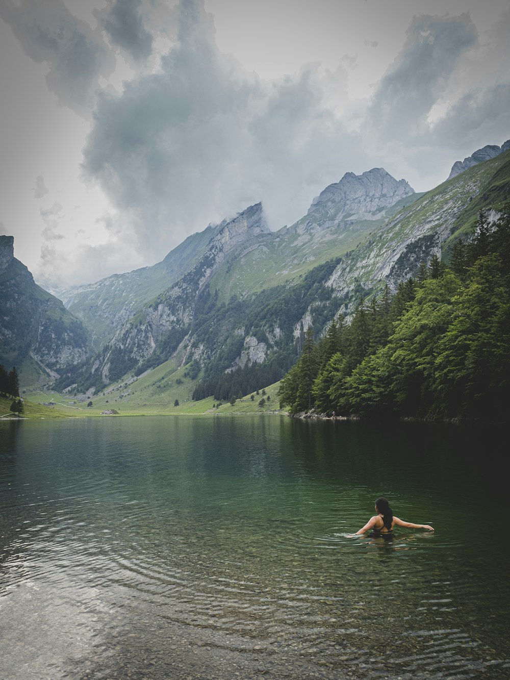 Frau im schwarzen Bikini sitzt tagsüber auf Felsen vor dem See