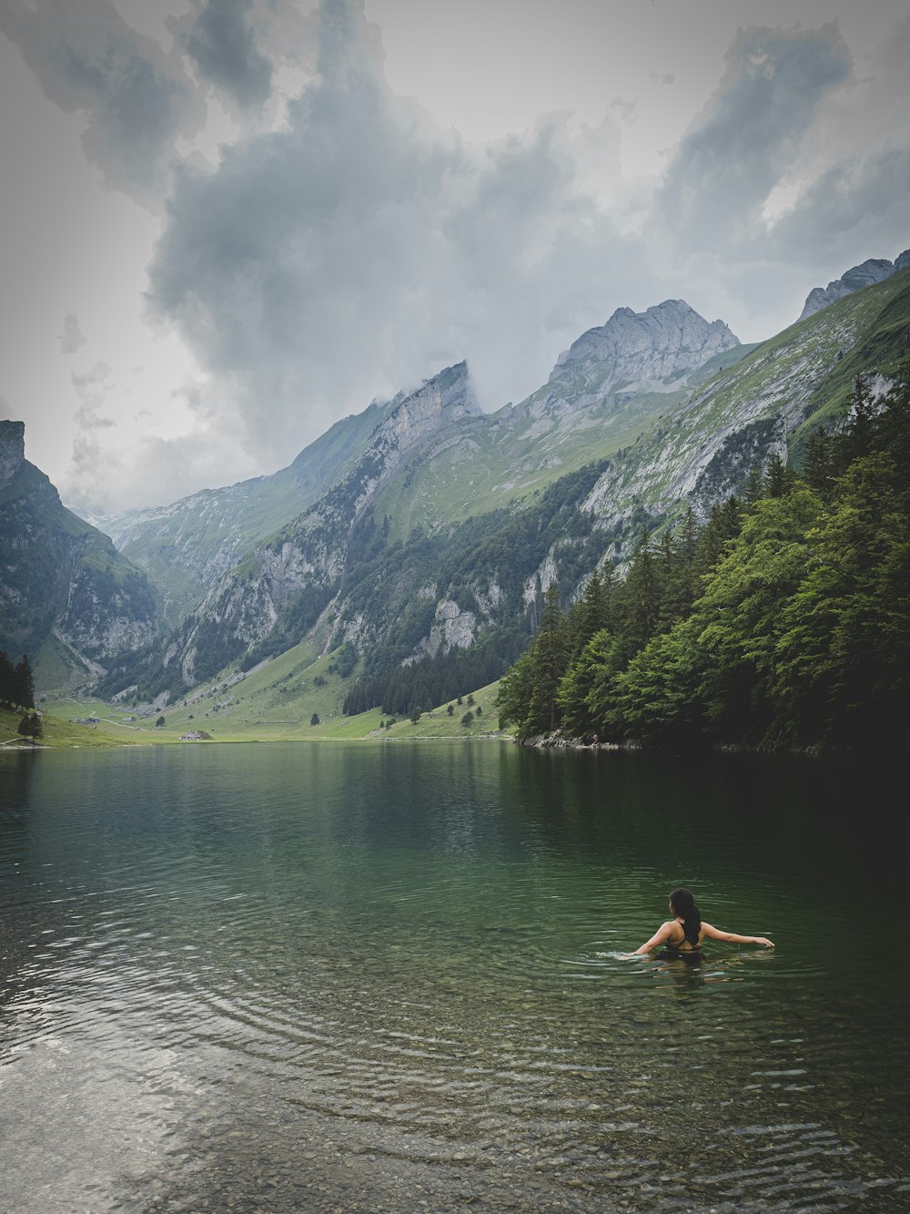 woman in black bikini sitting on rock in front of lake during daytime