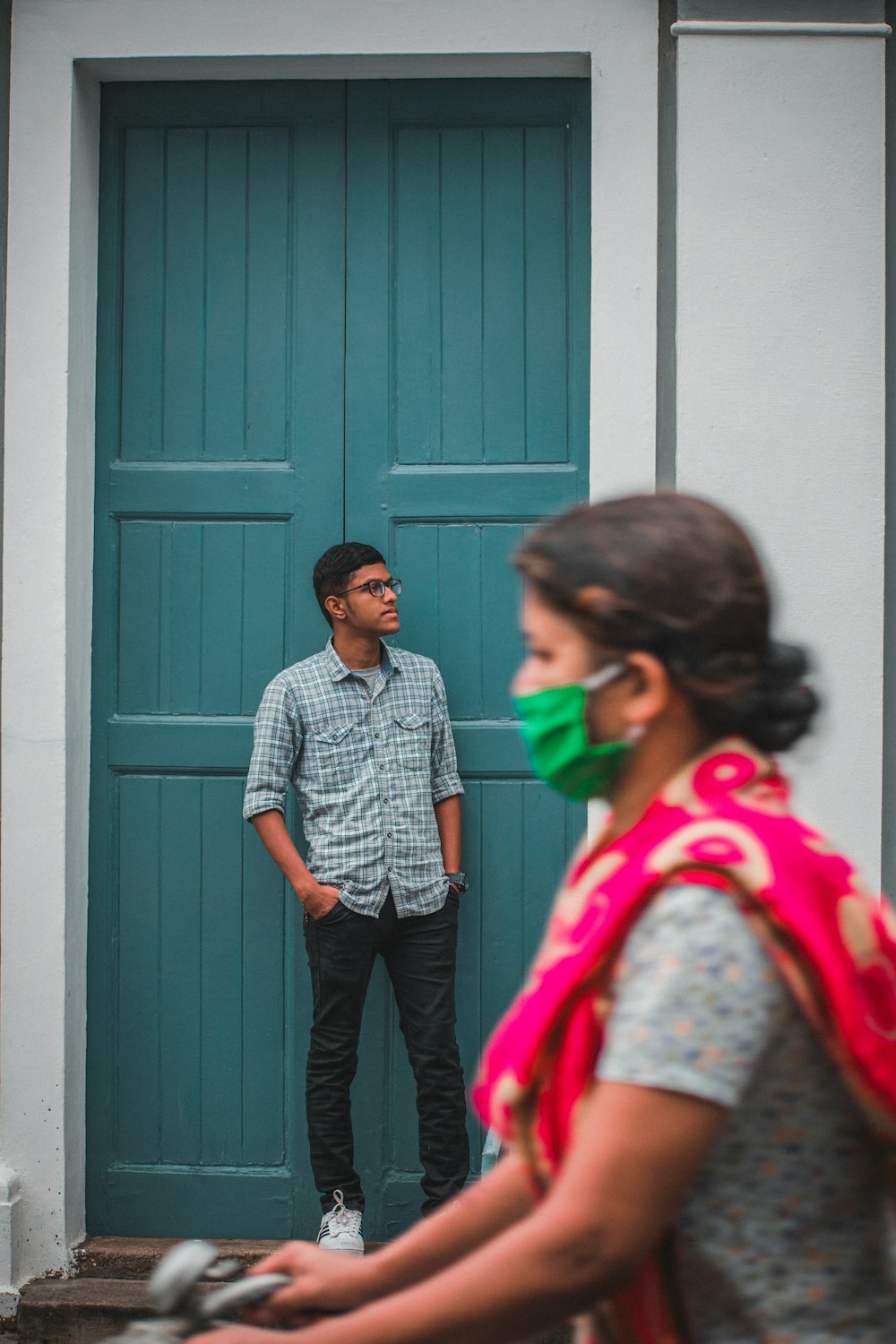 man in blue and white checkered dress shirt and black pants standing beside blue wooden door