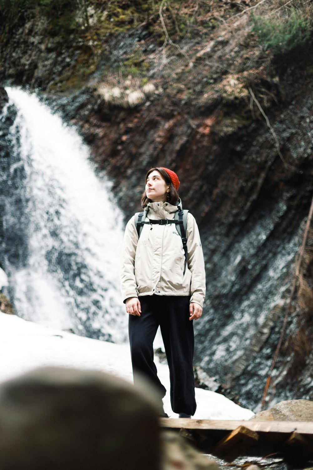 woman in gray jacket and black pants standing on rock formation near waterfalls during daytime
