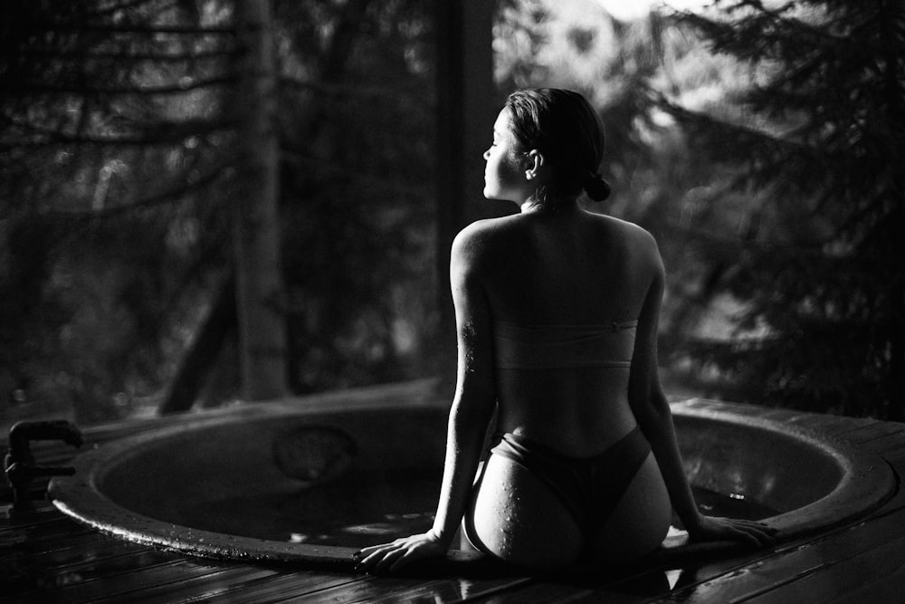 grayscale photo of woman in black bikini bottom sitting on pool