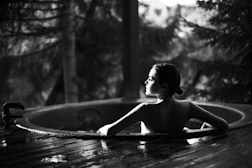 grayscale photo of topless woman sitting on wooden dock