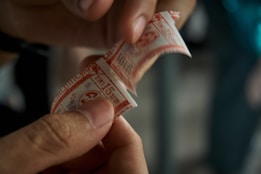 A hand is holding a small paper ticket, which has red and white colors with text and numbers printed on it.