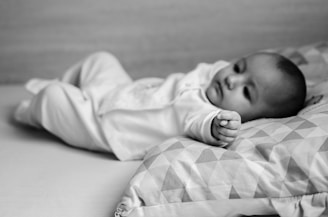 grayscale photo of baby in white onesie lying on bed