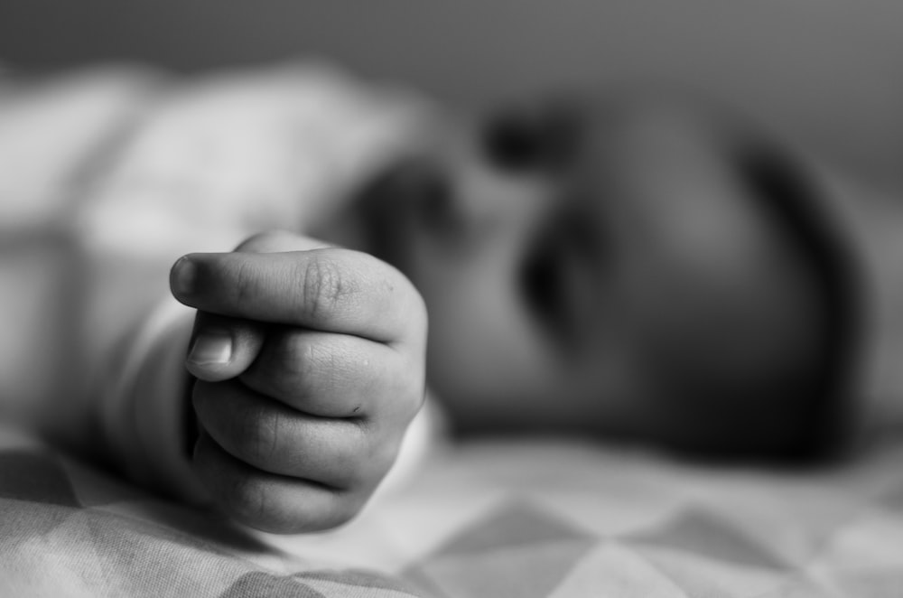 grayscale photo of baby lying on bed