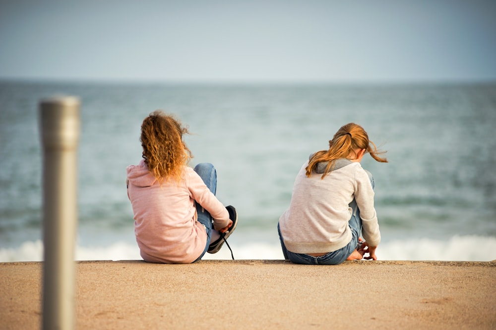 woman in pink long sleeve shirt sitting on brown sand near body of water during daytime