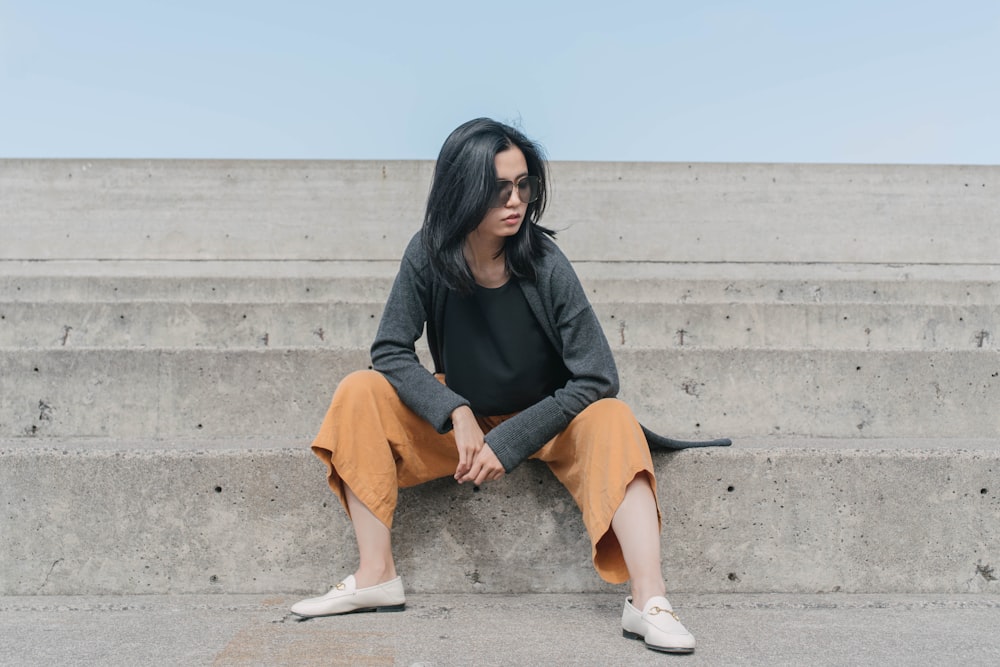 woman in black long sleeve shirt and brown skirt sitting on gray concrete bench during daytime