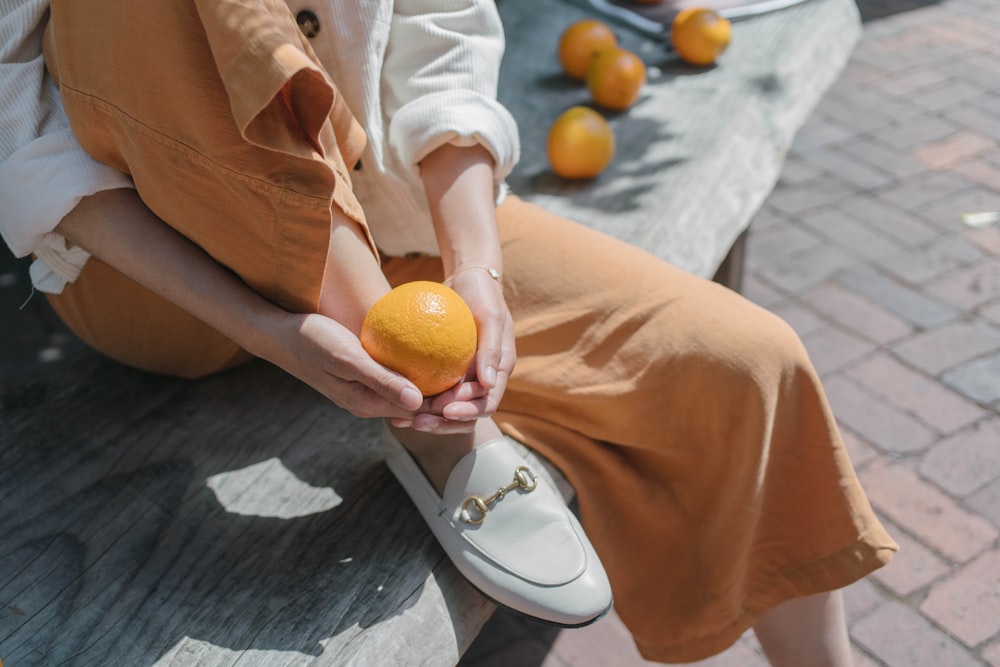 person in brown dress shirt holding orange fruit