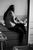 woman in white shirt and black pants sitting on bed