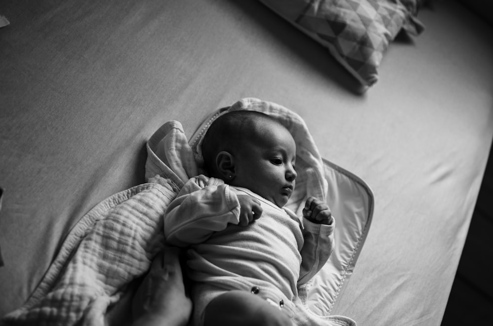 grayscale photo of baby lying on bed