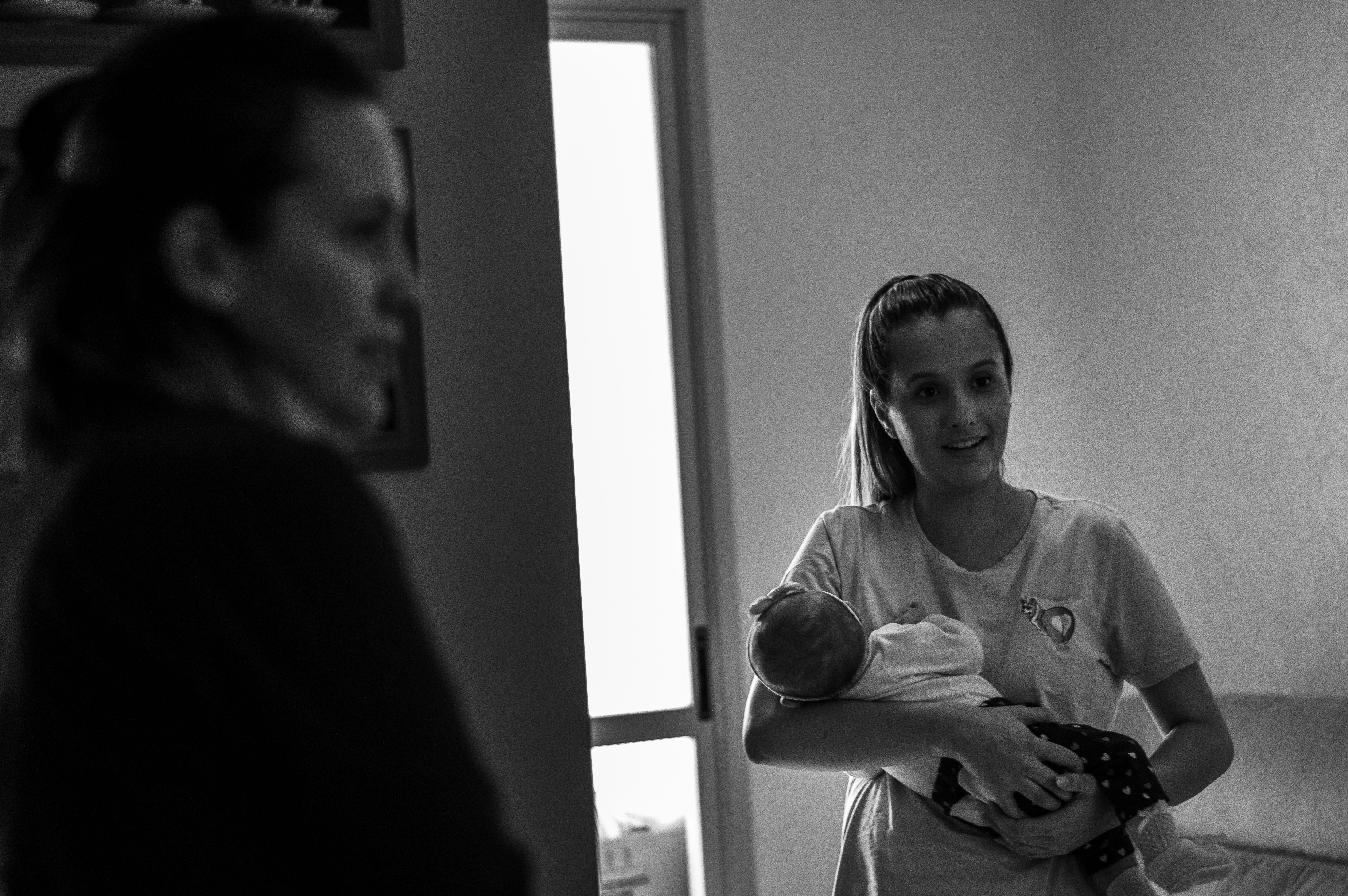 Midwife home visit — midwife supporting new parent holding baby during a home visit