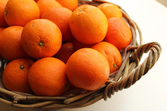 A rustic basket overflowing with freshly harvested oranges on a wooden table.