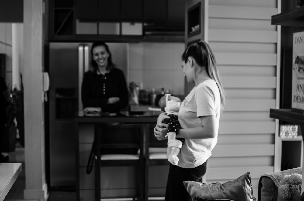 grayscale photo of woman in long sleeve shirt and pants holding glass bottle