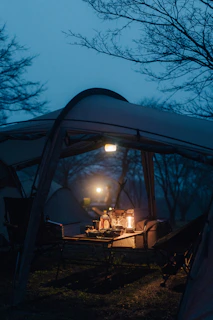 Aluminum folding camping table set up with gear and a warm orange lantern glowing softly