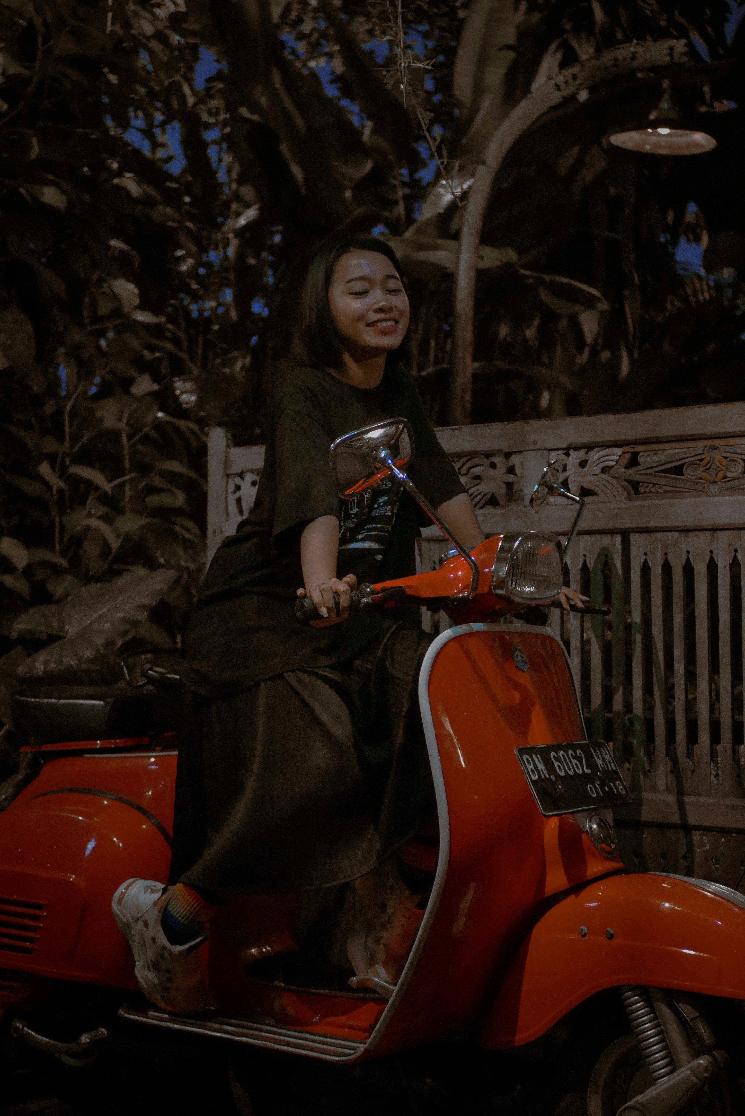 Wanita berjaket kulit hitam mengendarai skuter motor oranye