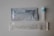The image displays components of a COVID-19 rapid antigen test kit. There is a sealed packet with branding and instructions, a small vial with a blue cap, and a packaged swab. The items are arranged on a light gray surface.